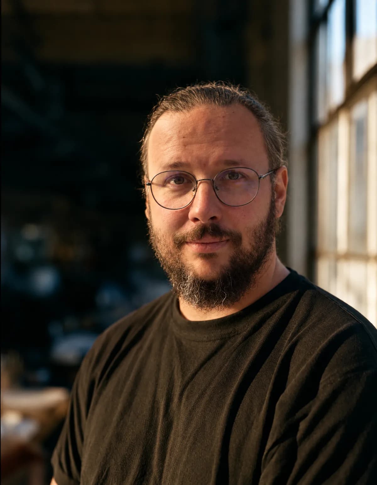 Tobias Vonau — Portrait in einer Werkstatt, Brille, dunkles Shirt, von der Seite durch ein Fenster beleuchtet